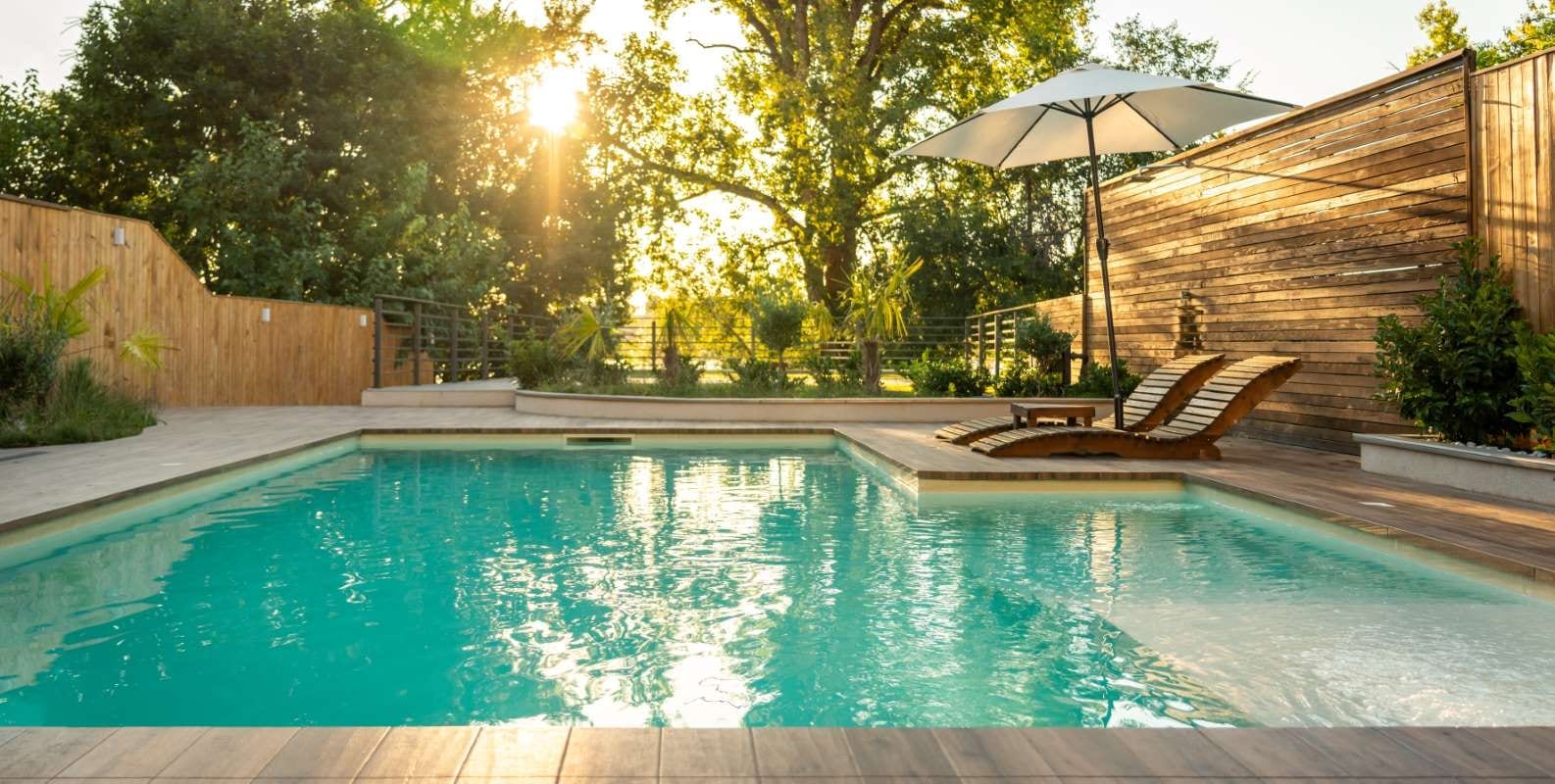 Sunset view of a luxury villa pool with wooden lounge chairs and serene opulence
